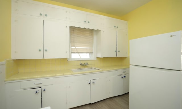 4915 Walker St, Houston, TX 77023 - kitchen featuring freestanding refrigerator, a sink, tasteful backsplash, tile counters, and white cabinets