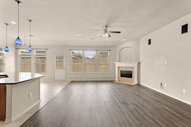 12906 Leafy Shores Dr, Houston, TX 77044 - unfurnished living room featuring ceiling fan, a textured ceiling, a tiled fireplace, wood finished floors, and baseboards