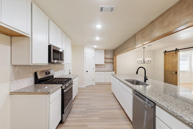 2801 Pickerton Dr, Deer Park, TX 77536 - kitchen with stainless steel appliances, a sink, a barn door, light wood finished floors, and decorative backsplash