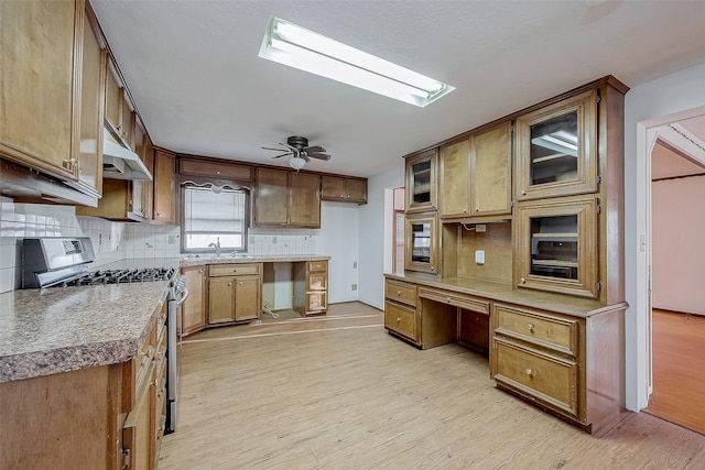 31002 Misty Meadow Dr, Magnolia, TX 77354 - kitchen featuring stainless steel range with gas cooktop, backsplash, light wood finished floors, under cabinet range hood, and glass insert cabinets