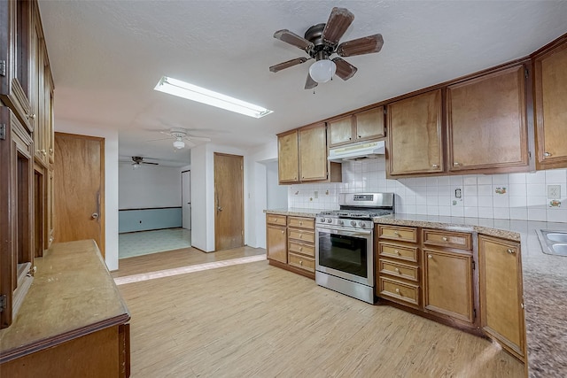 31002 Misty Meadow Dr, Magnolia, TX 77354 - kitchen with stainless steel gas stove, ceiling fan, under cabinet range hood, tasteful backsplash, and light wood-type flooring