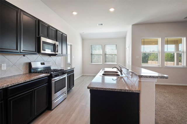 6502 Blimp Base Blvd, Hitchcock, TX 77563 - kitchen featuring stainless steel appliances, a sink, dark cabinetry, decorative backsplash, and a center island with sink