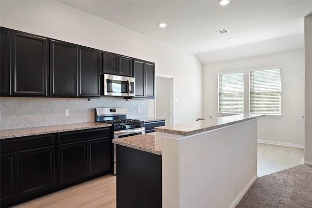 6502 Blimp Base Blvd, Hitchcock, TX 77563 - kitchen with appliances with stainless steel finishes, dark cabinetry, decorative backsplash, light stone countertops, and a center island with sink