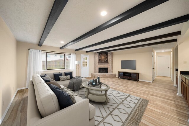 2311 Jackson Ln, League City, TX 77573 - living room with a brick fireplace, baseboards, beamed ceiling, light wood-style flooring, and a textured ceiling