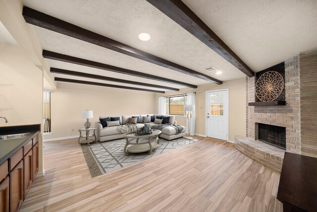 2311 Jackson Ln, League City, TX 77573 - living area featuring baseboards, beamed ceiling, a brick fireplace, light wood-style flooring, and a textured ceiling