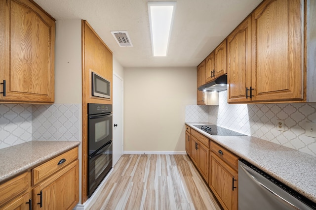 2311 Jackson Ln, League City, TX 77573 - kitchen with black appliances, under cabinet range hood, light wood finished floors, brown cabinetry, and decorative backsplash