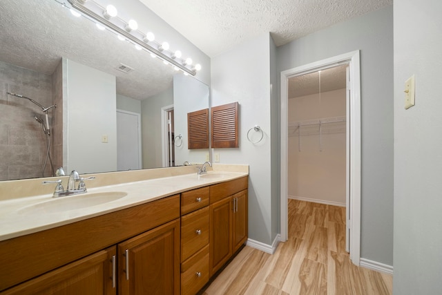 2311 Jackson Ln, League City, TX 77573 - bathroom with a textured ceiling, wood finished floors, double vanity, tiled shower, and a spacious closet