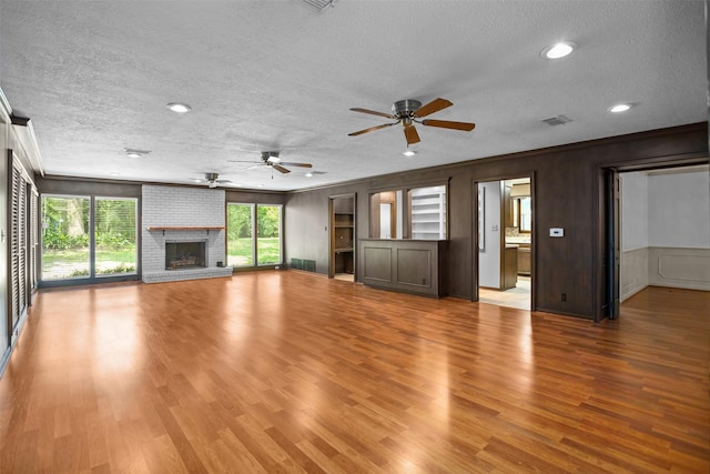 103 N Gordon Dr, Crockett, TX 75835 - unfurnished living room featuring a textured ceiling, a ceiling fan, a brick fireplace, light wood-style flooring, and ornamental molding
