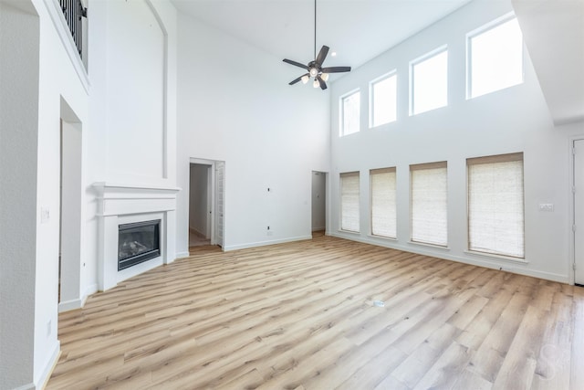 4131 Creek Shore Ln, Fulshear, TX 77441 - unfurnished living room with a towering ceiling, a ceiling fan, a glass covered fireplace, light wood-style floors, and baseboards