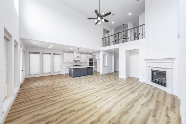 4131 Creek Shore Ln, Fulshear, TX 77441 - unfurnished living room featuring ceiling fan, light wood finished floors, recessed lighting, a towering ceiling, and a glass covered fireplace