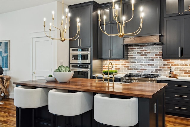 1514 31st St, Galveston, TX 77550 - kitchen featuring wooden counters, a chandelier, wood finished floors, appliances with stainless steel finishes, and an island with sink