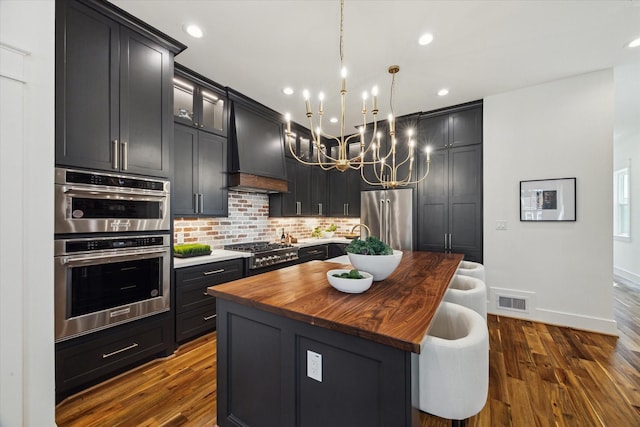1514 31st St, Galveston, TX 77550 - kitchen featuring stainless steel appliances, custom range hood, butcher block counters, a kitchen island with sink, and tasteful backsplash