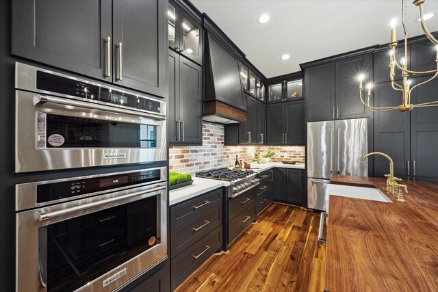 1514 31st St, Galveston, TX 77550 - kitchen featuring appliances with stainless steel finishes, custom exhaust hood, dark wood-style floors, tasteful backsplash, and glass insert cabinets
