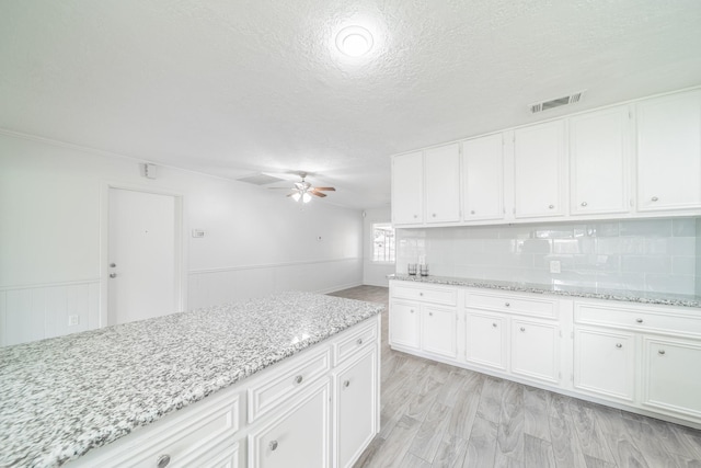 5229 W 43rd St, Houston, TX 77092 - kitchen with a textured ceiling, a ceiling fan, white cabinetry, light stone countertops, and wainscoting