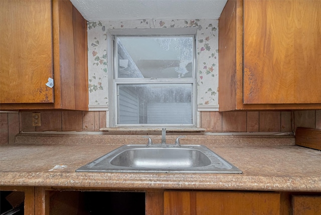 13326 Sundale Rd, Houston, TX 77038 - kitchen featuring wallpapered walls, a sink, brown cabinetry, light countertops, and a textured ceiling