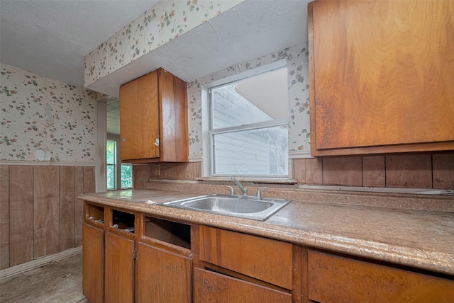 13326 Sundale Rd, Houston, TX 77038 - kitchen featuring wallpapered walls, a sink, a wainscoted wall, brown cabinetry, and light countertops