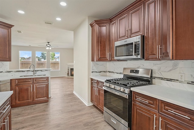 19326 Camellia Knoll Trl, Houston, TX 77084 - kitchen featuring stainless steel appliances, a sink, a ceiling fan, backsplash, and light wood-style flooring