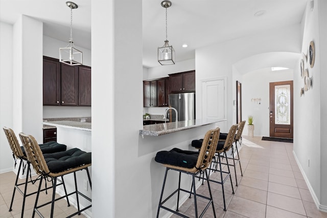 2807 Hadley Spgs, Spring, TX 77386 - kitchen featuring stainless steel refrigerator, arched walkways, a kitchen breakfast bar, light tile patterned floors, and dark brown cabinetry