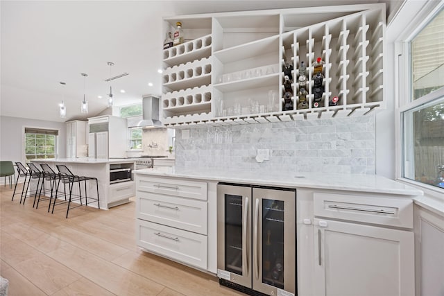 18215 Hereford Ln, Houston, TX 77058 - indoor dry bar featuring beverage cooler, wall chimney exhaust hood, tasteful backsplash, light wood finished floors, and recessed lighting