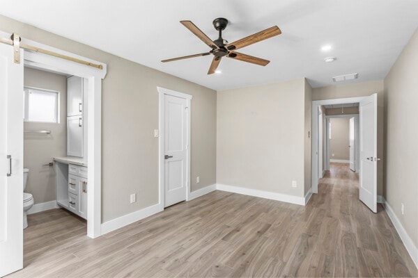 10719 Carlota Ct, Houston, TX 77096 - unfurnished bedroom with light wood-type flooring, a barn door, ensuite bathroom, and a ceiling fan