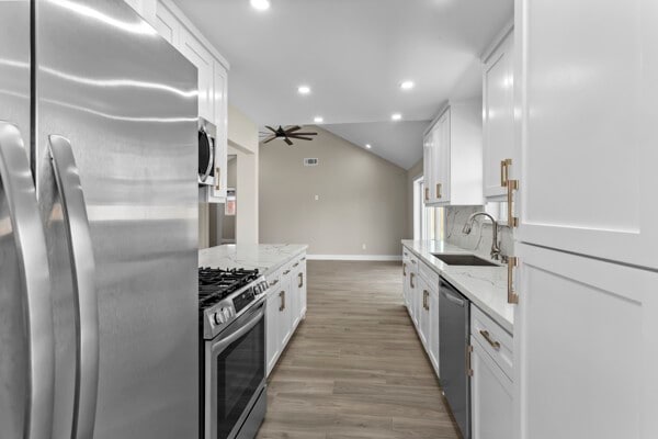 10719 Carlota Ct, Houston, TX 77096 - kitchen with appliances with stainless steel finishes, a sink, baseboards, white cabinetry, and light wood-type flooring