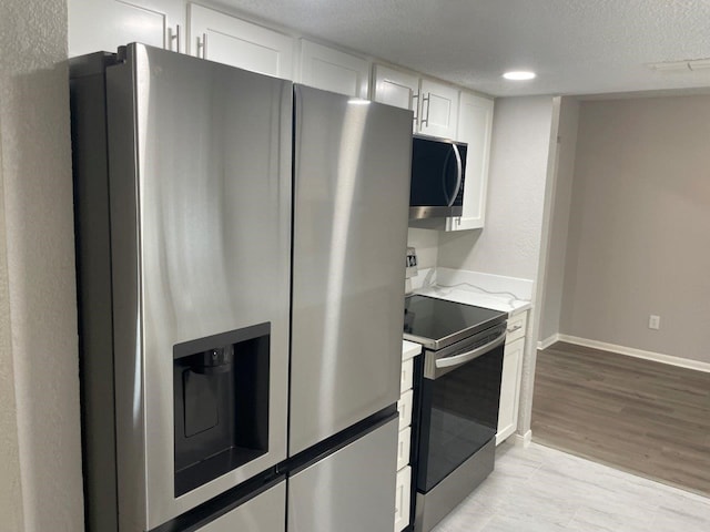19414 Leafwood Ln, Houston, TX 77084 - kitchen with appliances with stainless steel finishes, white cabinetry, baseboards, a textured ceiling, and light wood finished floors
