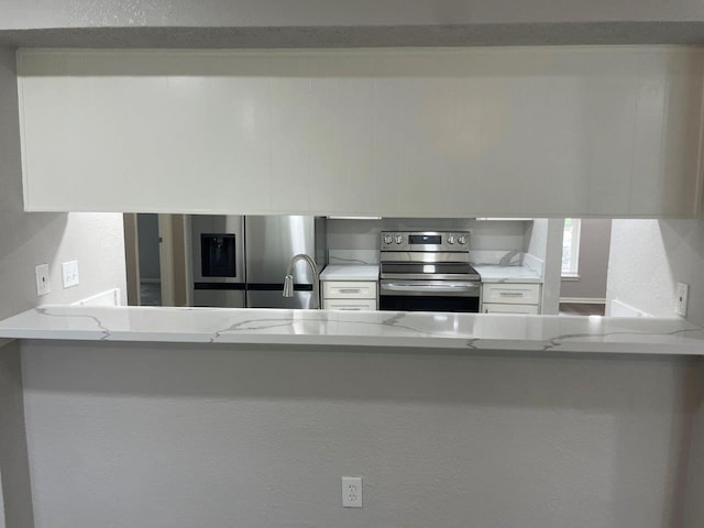 19414 Leafwood Ln, Houston, TX 77084 - kitchen featuring appliances with stainless steel finishes, white cabinetry, a peninsula, and light stone countertops