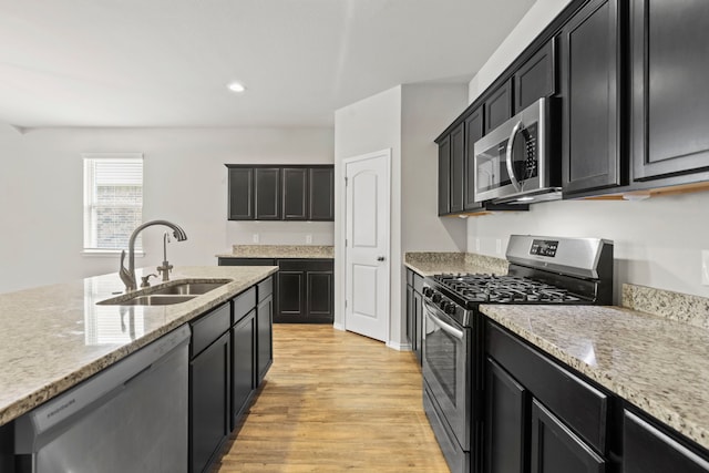 18061 Atwood Mill Dr, New Caney, TX 77357 - kitchen featuring appliances with stainless steel finishes, a sink, dark cabinetry, light wood finished floors, and recessed lighting