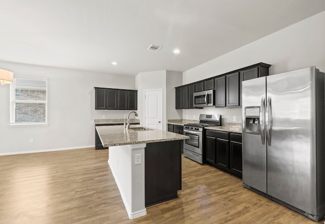 18061 Atwood Mill Dr, New Caney, TX 77357 - kitchen featuring stainless steel appliances, a sink, light stone countertops, light wood finished floors, and a kitchen island with sink