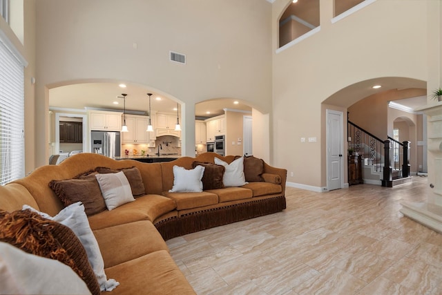 19023 Wild Thornberry Dr, Tomball, TX 77377 - living area featuring arched walkways, a towering ceiling, light marble finish floors, stairs, and baseboards