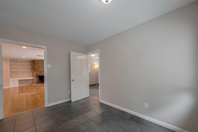 10126 Whiteside Ln, Houston, TX 77043 - empty room with a brick fireplace, baseboards, built in shelves, and dark tile patterned floors