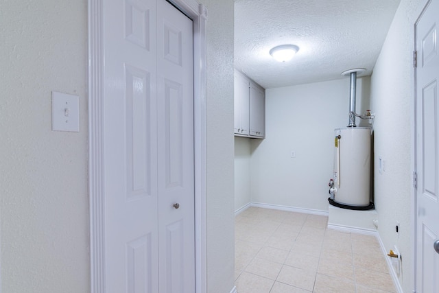 5214 Meadow Crest St, La Porte, TX 77571 - laundry area featuring water heater, cabinet space, a textured ceiling, light tile patterned flooring, and baseboards