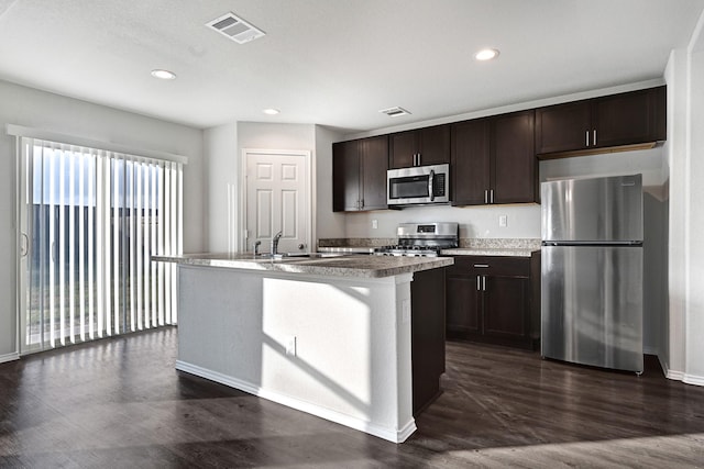 4354 Tulip Oak Dr, Houston, TX 77068 - kitchen featuring stainless steel appliances, dark brown cabinetry, dark wood finished floors, a kitchen island with sink, and recessed lighting