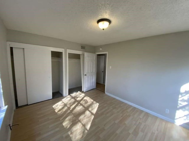 5810 Belmark St, Houston, TX 77033 - unfurnished bedroom featuring two closets, a textured ceiling, light wood-style floors, and baseboards