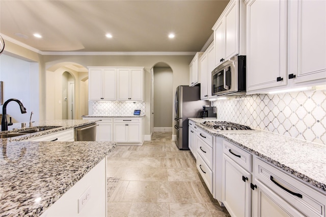 28907 Copper Break Ct, Katy, TX 77494 - kitchen with appliances with stainless steel finishes, arched walkways, a sink, white cabinetry, and ornamental molding