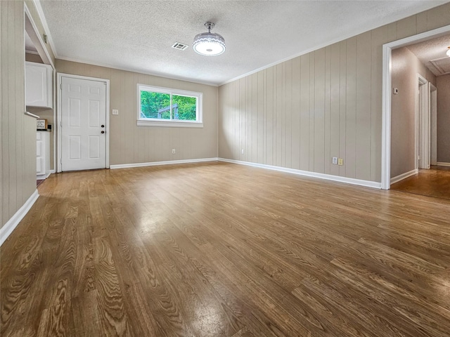 723 Pas Trl, Houston, TX 77336 - unfurnished living room featuring wood finished floors, a textured ceiling, baseboards, ornamental molding, and wooden walls