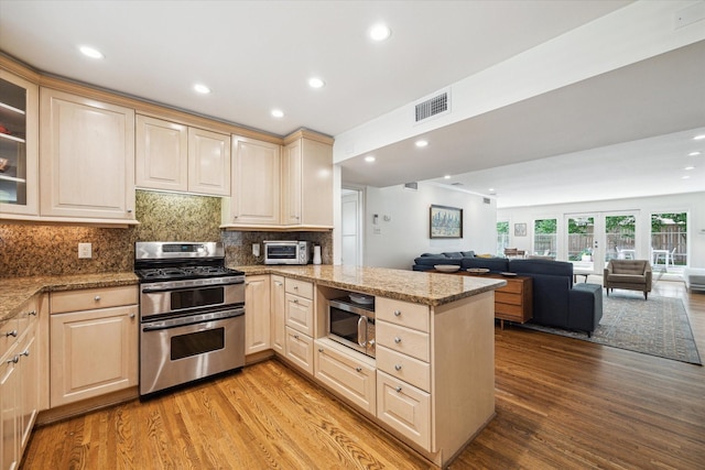 2415 Avalon Pl, Houston, TX 77019 - kitchen with stainless steel appliances, a peninsula, open floor plan, light brown cabinetry, and light wood finished floors