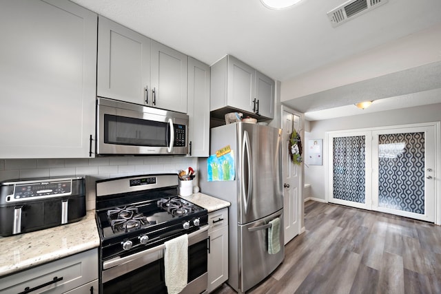 3808 Cottonwood Dr, La Porte, TX 77571 - kitchen with stainless steel appliances, decorative backsplash, wood finished floors, gray cabinets, and light stone countertops