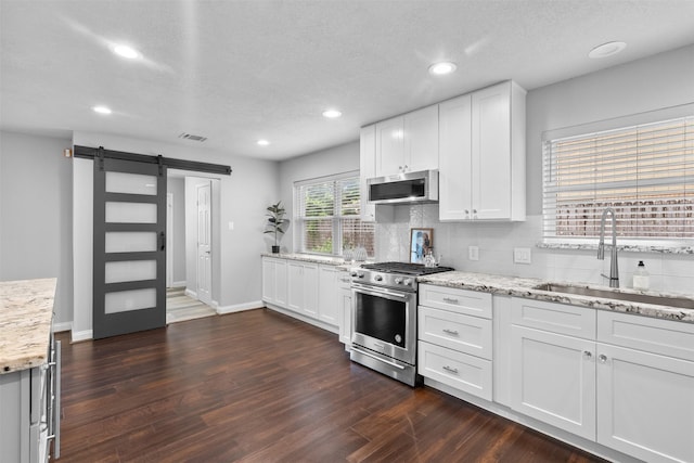 1139 Lehman St, Houston, TX 77018 - kitchen featuring stainless steel appliances, a sink, a barn door, dark wood-style flooring, and backsplash
