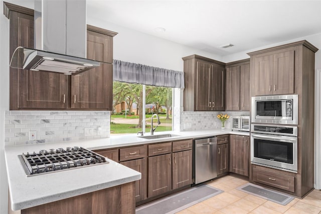 1706 Brightlake Way, Missouri City, TX 77459 - kitchen featuring appliances with stainless steel finishes, island exhaust hood, a sink, tasteful backsplash, and light tile patterned floors