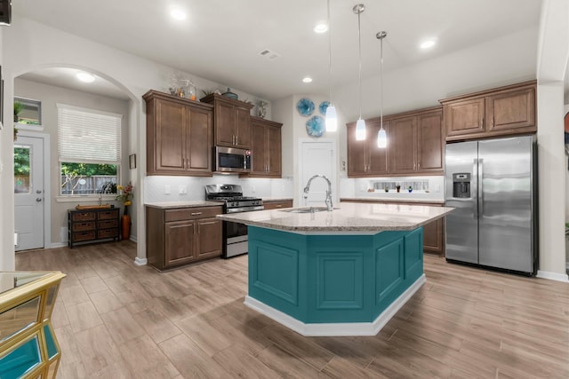 371 Westlake Terrace Dr, Conroe, TX 77304 - kitchen featuring appliances with stainless steel finishes, a sink, arched walkways, hanging light fixtures, and a center island with sink