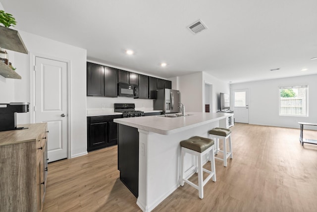 18107 Rockvine Dr, Hockley, TX 77447 - kitchen with black appliances, a sink, light wood finished floors, a center island with sink, and a breakfast bar area
