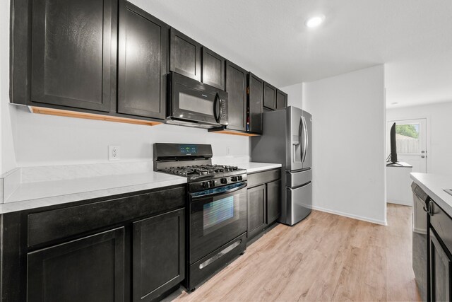18107 Rockvine Dr, Hockley, TX 77447 - kitchen featuring black appliances, light wood finished floors, light countertops, dark cabinetry, and baseboards