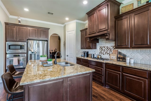 10040 Easton Sky Ln, Cypress, TX 77433 - kitchen with stainless steel appliances, arched walkways, a sink, light stone countertops, and a kitchen island with sink