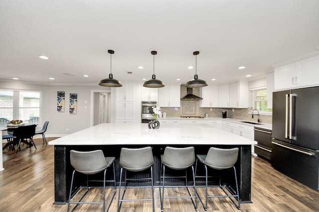 7519 Foster Creek Dr, Richmond, TX 77406 - kitchen with appliances with stainless steel finishes, wall chimney range hood, a large island, decorative backsplash, and white cabinetry