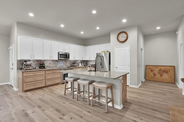 9203 White Tail Dr, Conroe, TX 77303 - kitchen with stainless steel appliances, backsplash, a kitchen island with sink, light wood-style floors, and a breakfast bar