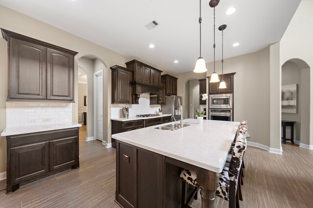 2506 Haven Hill Dr, Katy, TX 77494 - kitchen with arched walkways, stainless steel appliances, a sink, dark brown cabinetry, and tasteful backsplash