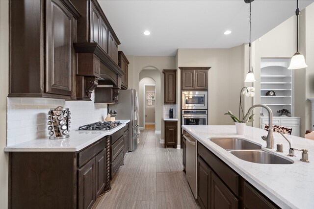 2506 Haven Hill Dr, Katy, TX 77494 - kitchen featuring stainless steel appliances, a sink, dark brown cabinets, arched walkways, and decorative backsplash