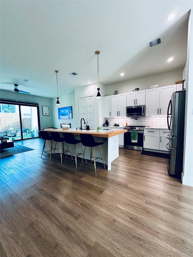 210 E 39th St, Houston, TX 77018 - kitchen featuring appliances with stainless steel finishes, dark wood-type flooring, butcher block counters, a center island with sink, and white cabinets