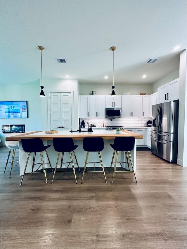 210 E 39th St, Houston, TX 77018 - kitchen featuring stainless steel appliances, white cabinetry, light countertops, decorative backsplash, and a breakfast bar area
